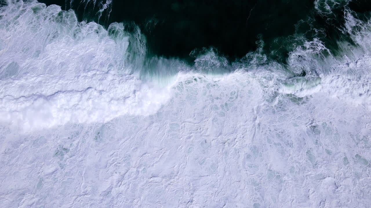 Crashing Atlantic wave leaves white wash and patterns; aerial tilt-down riser