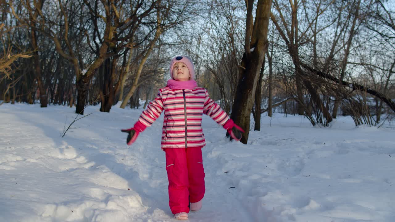 niño alegre niño corriendo, divirtiéndose, bailando, tonto en el camino nevado en el bosque del parque de invierno
