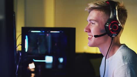 niño adolescente que usa auriculares jugando en casa usando dos pantallas de computadora