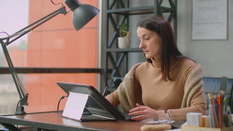una diseñadora gráfica trabaja en una oficina con grandes ventanas y pinta usando un lápiz y una pantalla táctil de computadora. estación de trabajo con pantalla táctil para diseñadores. idear y desarrollar el concepto del logotipo.