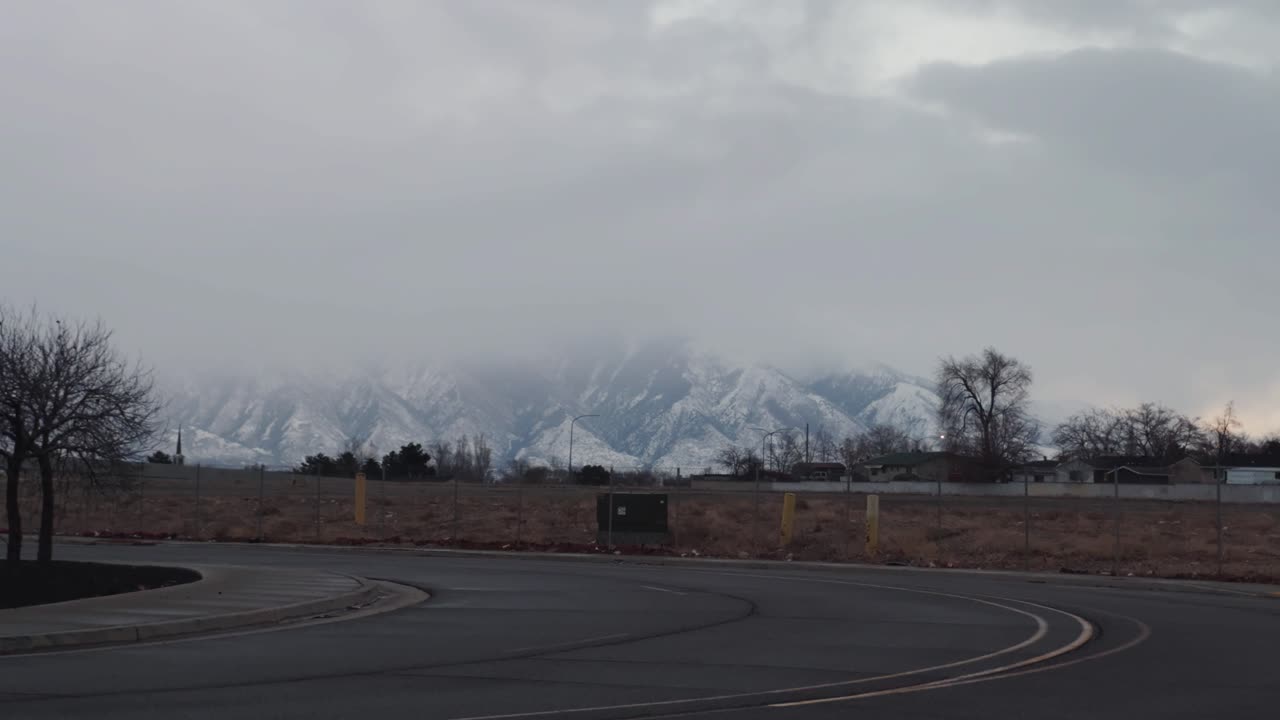 Slowly panning right to left on an empty street with a neighborhood in the close background and snow covered mountains in the distance on a cloudy winter day in Utah.