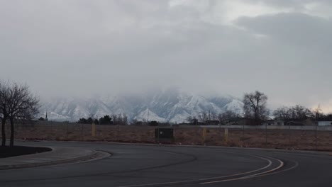 slowly panning right to left on an empty street with a neighborhood in the close background and snow covered mountains in the distance on a cloudy winter day in utah.