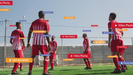 Animation-of-social-media-icons-over-team-of-diverse-male-soccer-players-practicing-on-sports-field