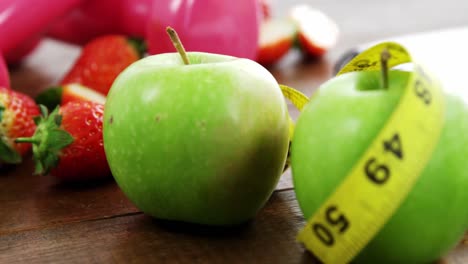 pesas y frutas con cinta de medición en una mesa de madera