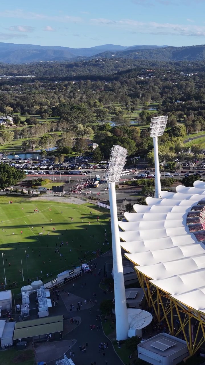 High-angle drone shot pans across a large sports stadium and lush green landscape under sunlight.