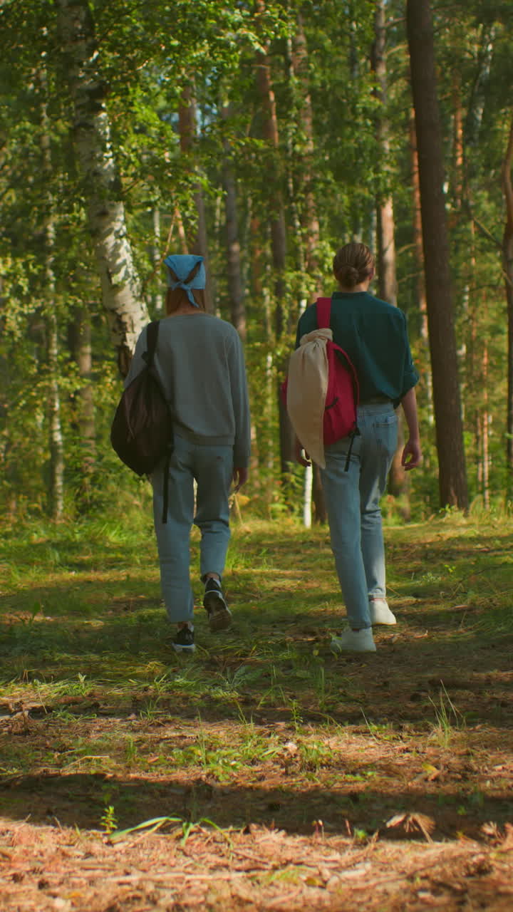 Back view of two young women with backpacks walking together through ...