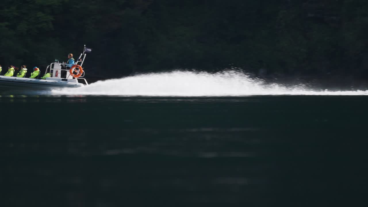 A speedboat carrying passengers in safety gear races through the calm waters of Geiranger Fjord.