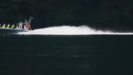 a speedboat carrying passengers in safety gear races through the calm waters of geiranger fjord.