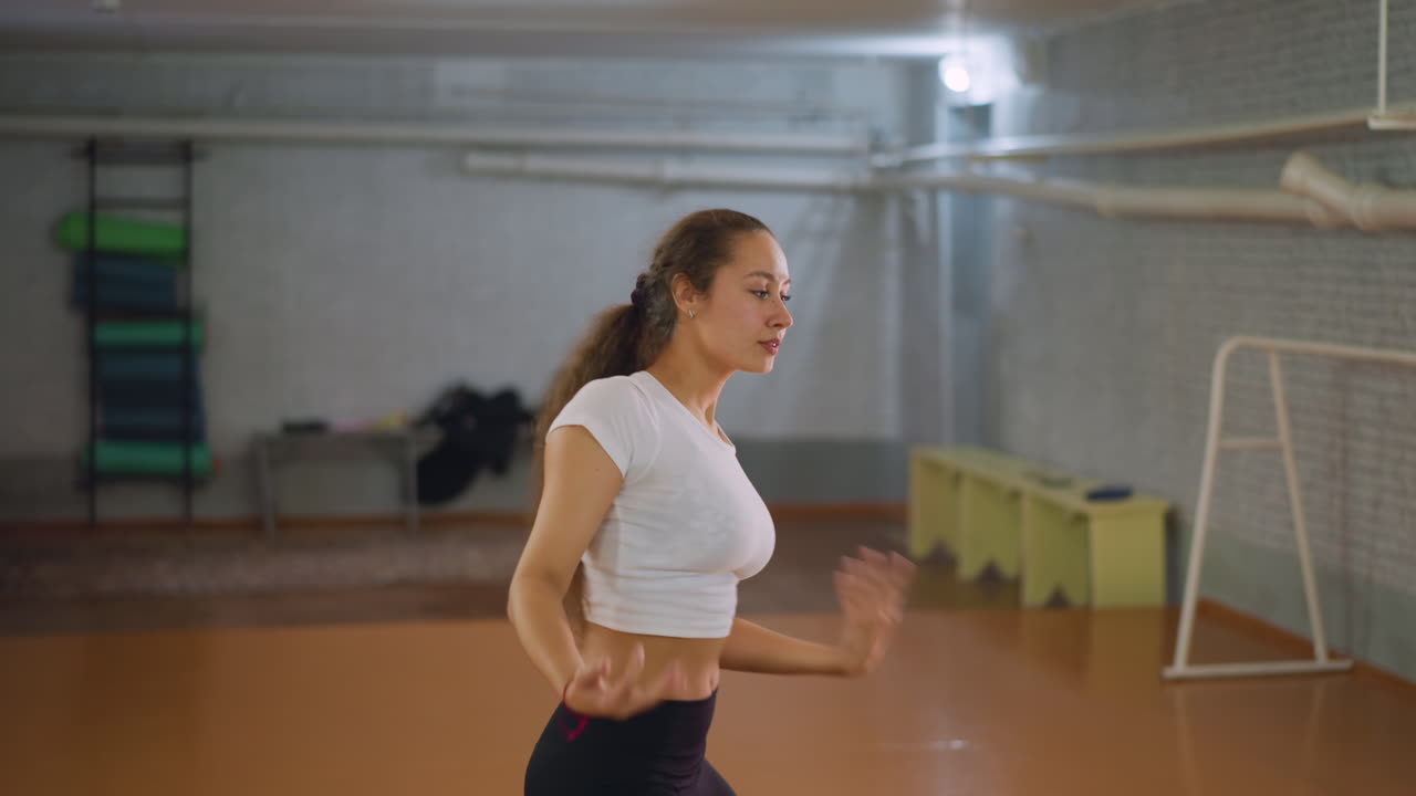 Woman in white top and black leggings exercising body while stretching arm in fitness studio, showing strength, endurance, and focus during workout routine with natural effort and determination