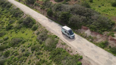 camper van driving along an old road between hills covered with bushes and greenery