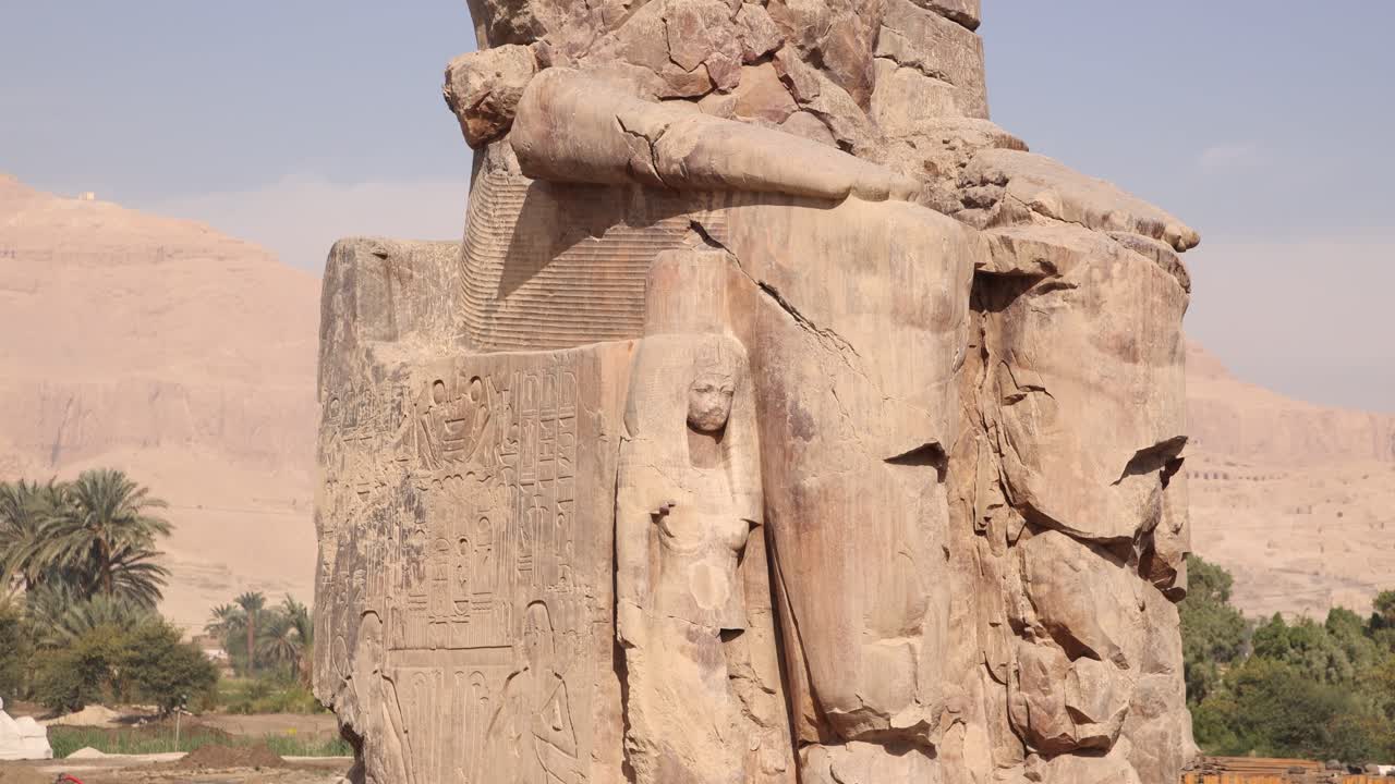 ruinas de la estatua gigante de faraón con montañas en el fondo en los colosos de memnon en luxor egipto con palma