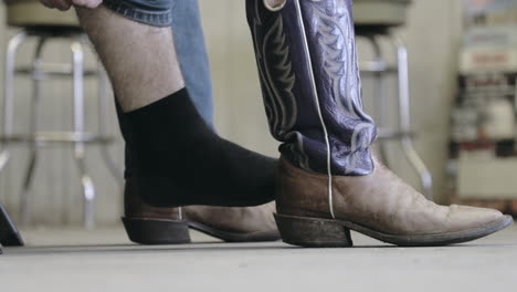 Sitting-man-putting-on-cowboy-boots-and-pulling-jeans-over-in-slow-motion