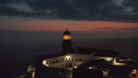 Aerial-circling-around-sensational-lighthouse-in-Lagos-Algarve,-Portugal,-light-flashing-at-dusk