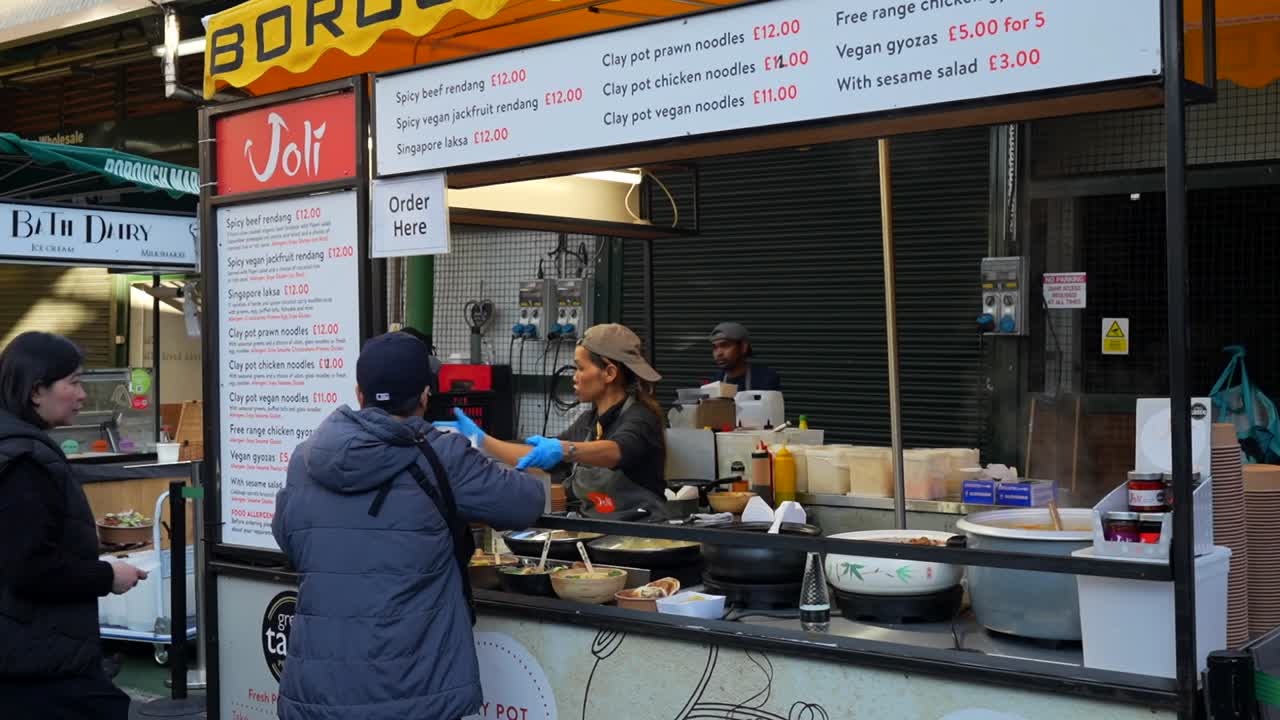 Tourists at Borough Market in London buy Asian street food as vendor gives directions for seating