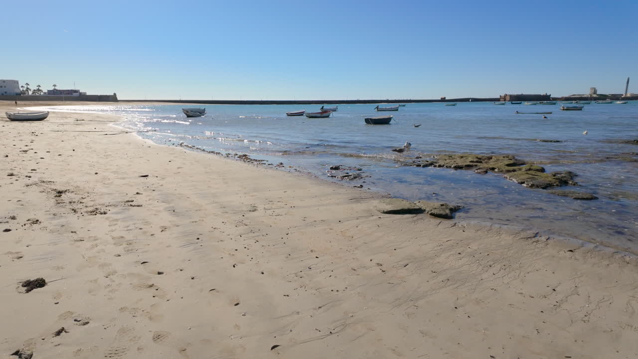 Small boats resting on the sandy shore with calm sea waters in C&aacute;diz, Spain