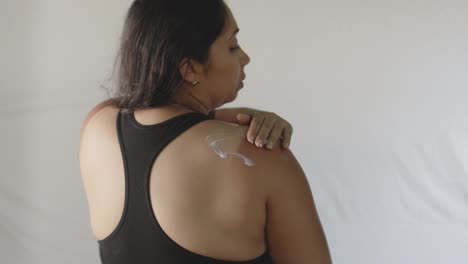 latin adult woman applying cream to the reddened skin of her sunburned back and shoulder