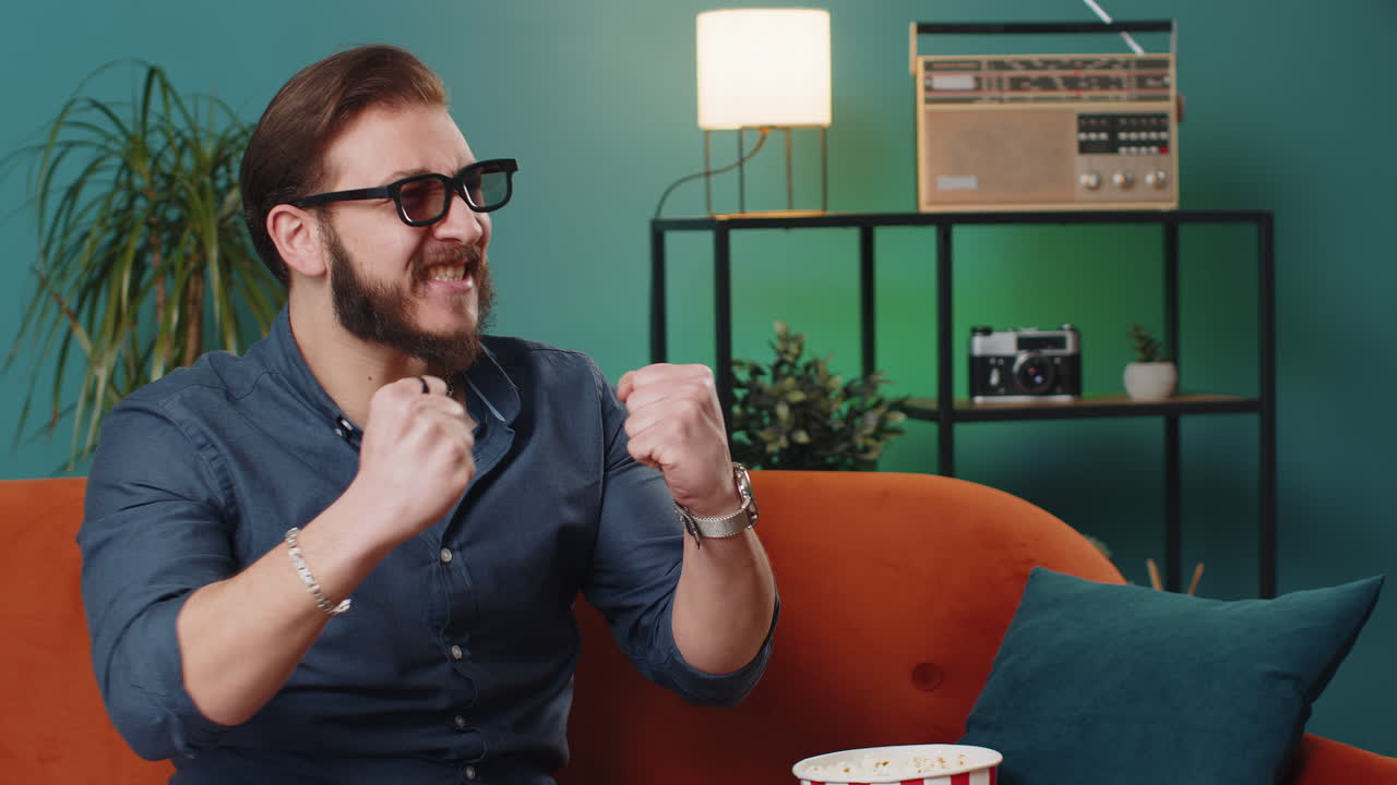 Lebanese man sits on sofa eating popcorn watching interesting tv serial sport game online at home