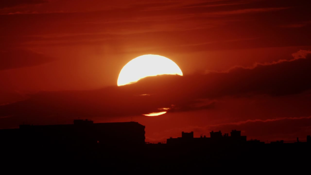 Golden sunset descending behind a dense urban skyline, silhouetting mid-rise residential buildings