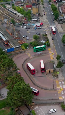 smooth drone orbit of chingford bus terminal and train station in east london, featuring red and green double-decker buses and train in the station. this station is where the line terminates