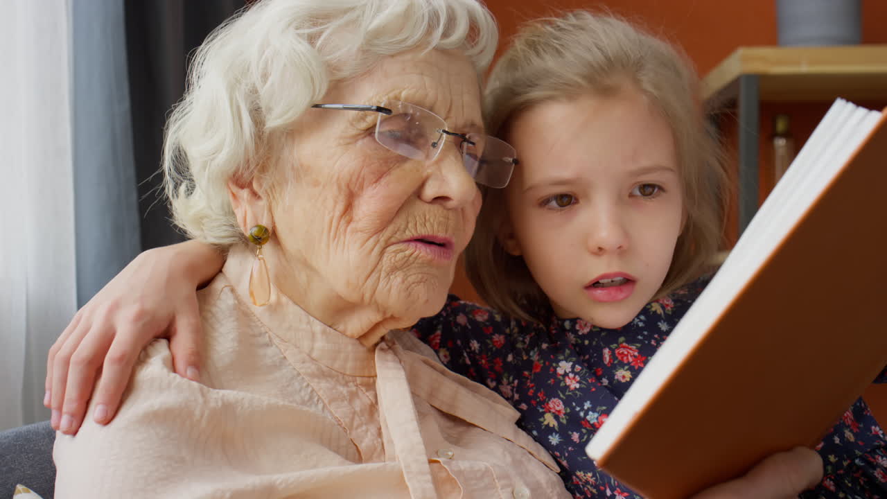 Little Girl Reading Book with Grandmother at Home