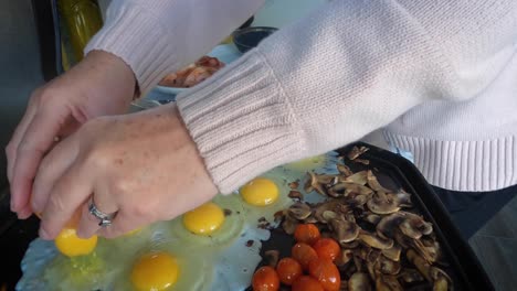 a mature pretty lady is cracking eggs on a hot barbecue while preparing a fried family brunch