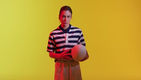 retrato de una jugadora de rugby caucásica con una pelota de rugby sobre iluminación amarilla de neón