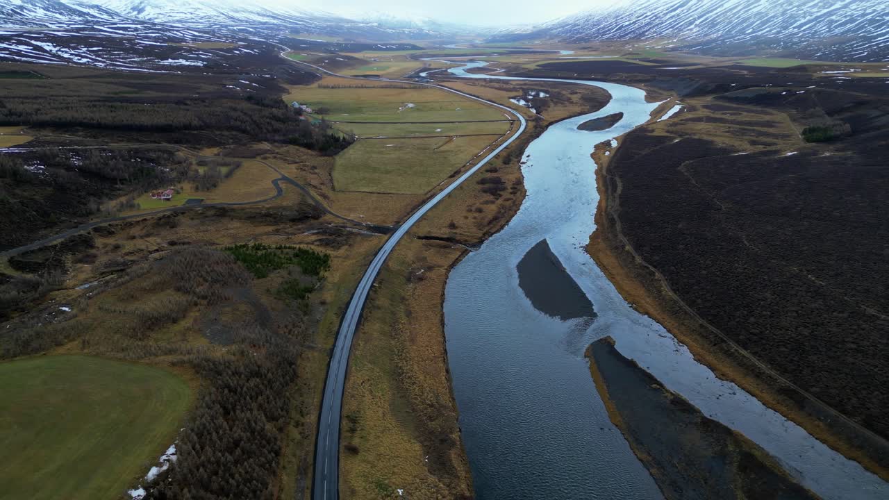 carretera aislada junto al río en un amplio valle con montañas nevadas aérea