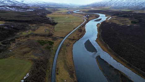 isolated road next river in broad valley with snowy mountains aerial