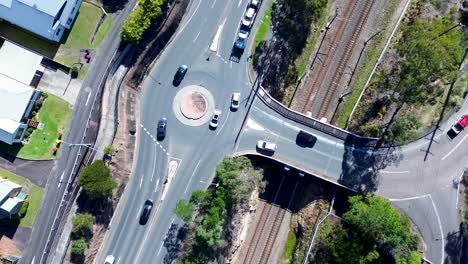 Panorámica-Sobre-El-Paisaje-Automóviles-Circulando-Por-La-Rotonda-Calle-Principal-Con-Línea-De-Tren-Puente-Infraestructura-Transporte-Ourimbah-Australia-Drone-Aéreo