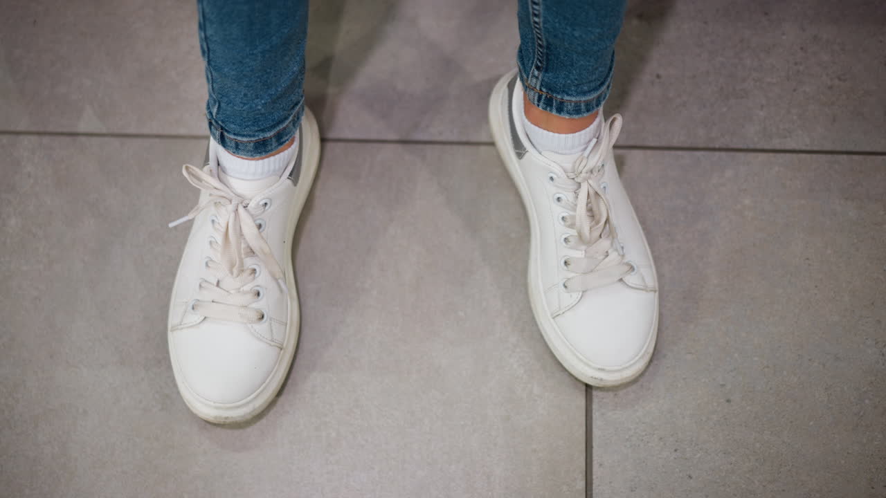 쇼핑몰의 깨한 타일로 된 바닥에 놓인 여성의  캔버스 스니커와 청바지 바지를 가까이 어 편안한 신발을 표시하고 오른발을 합니다.