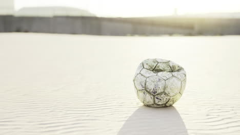 una pelota de fútbol desgastada descansando en una playa de arena durante la puesta de sol en una luz cálida