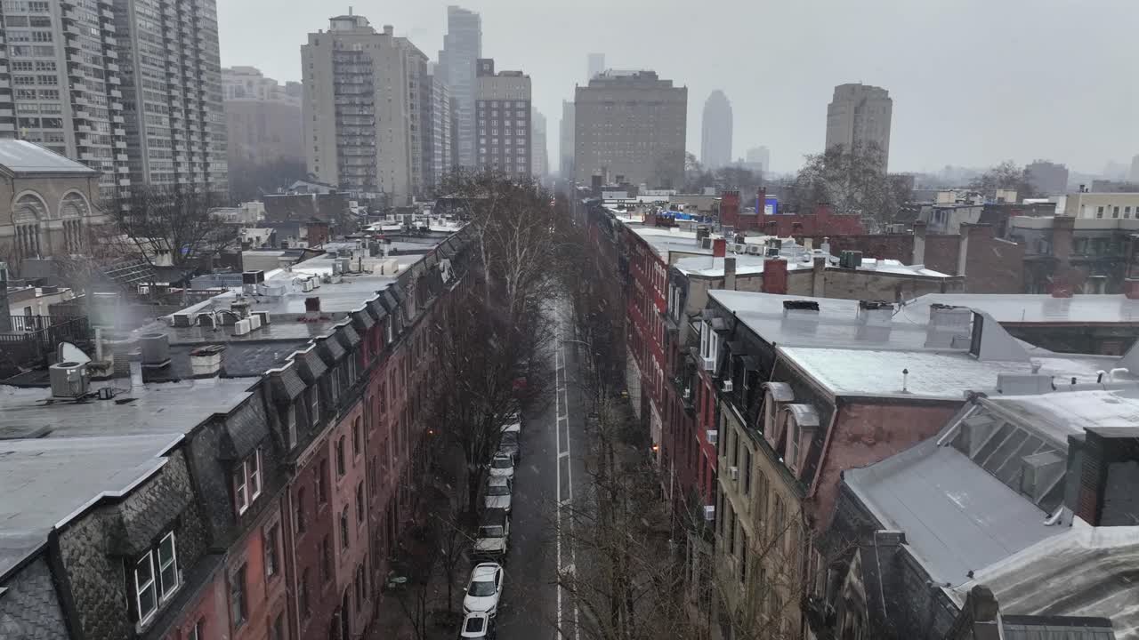 Luftfoto af Philadelphias centrum, der viser tætte rækkehusblokke og snedækkede hustage under grå vinterhimmel. Urbant boligbybillede med gader, parkerede biler og skyline i baggrunden. Overflyvning