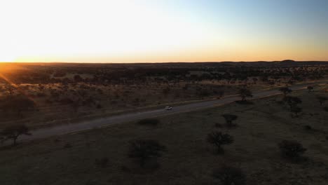 Aerial-view-following-a-car-driving-in-remote-wild,-sunny-evening-in-Namibia,-Africa