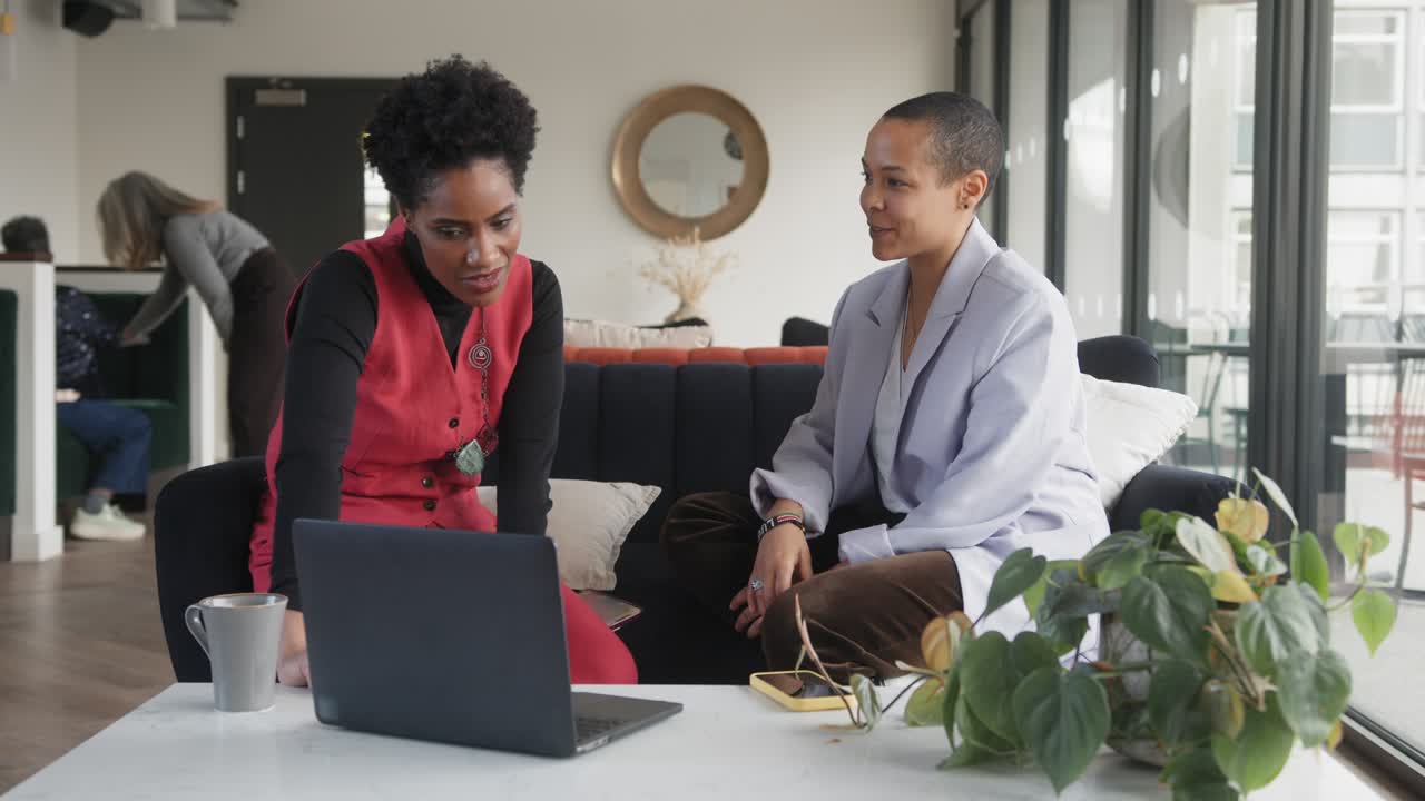 Slow motion of mixed race LGBTQ mid adult woman and mature black woman using laptop in office