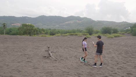 couple exploring volcanic black sand beach with mountains in background
