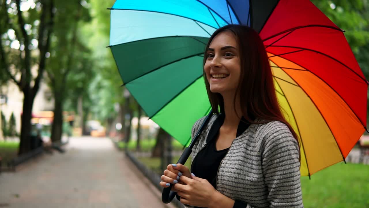 retrato de una joven sonriente girando su colorido paraguas y quitándolo porque ya no está lloviendo mirando