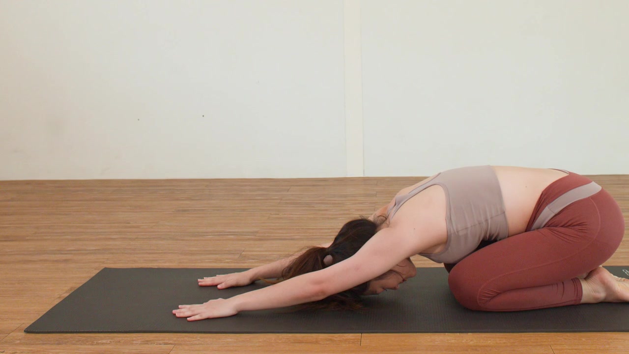 Donna asiatica esegue la posizione del bambino (Balasana) su un tappetino nero in uno studio luminoso