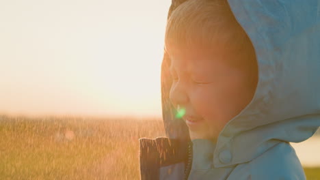 kid squints eyes under rain sprays outdoors happy little boy in hooded raincoat stands under