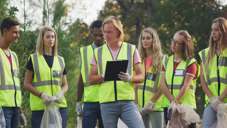 adultos con chaleco amarillo voluntarios y hombre tomando notas durante el día de limpieza del río