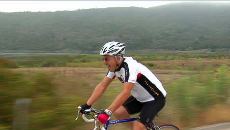 a bicyclist pants and grimaces as he peddles along a highway