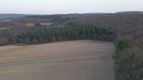 Brown-wheat-fields-surrounded-by-large-patches-of-coniferous-und-deciduous-forests-during-a-cloudy-sunset