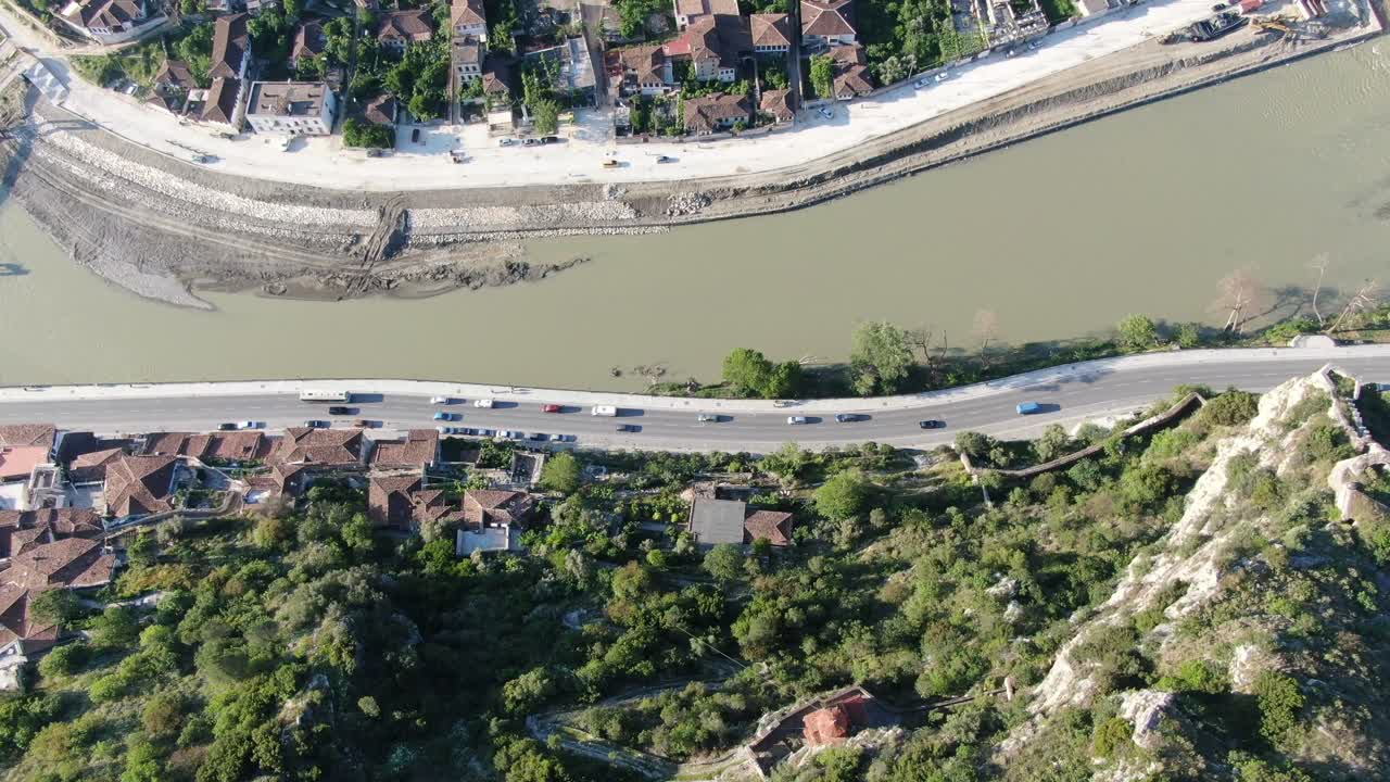 Vista aerea con drone in Albania che sorvola la città medievale di Berat, mostrando case in mattoni, un fiume e una montagna.