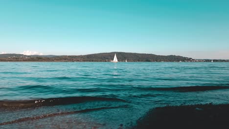 Cinematic-teal-colored-low-angle-view-of-yacht-cruise-in-calm-open-lake-waters-of-Maggiore-lake-in-Italy