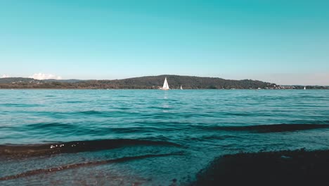 cinematic teal colored low-angle view of yacht cruise in calm open lake waters of maggiore lake in italy