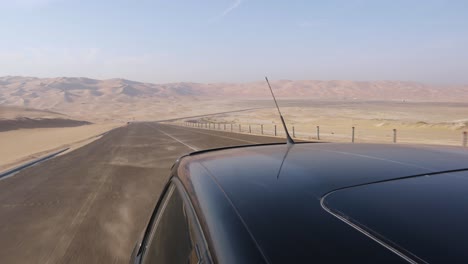 looking behind over rooftop of black car driving through spectacular empty abu dhabi desert road