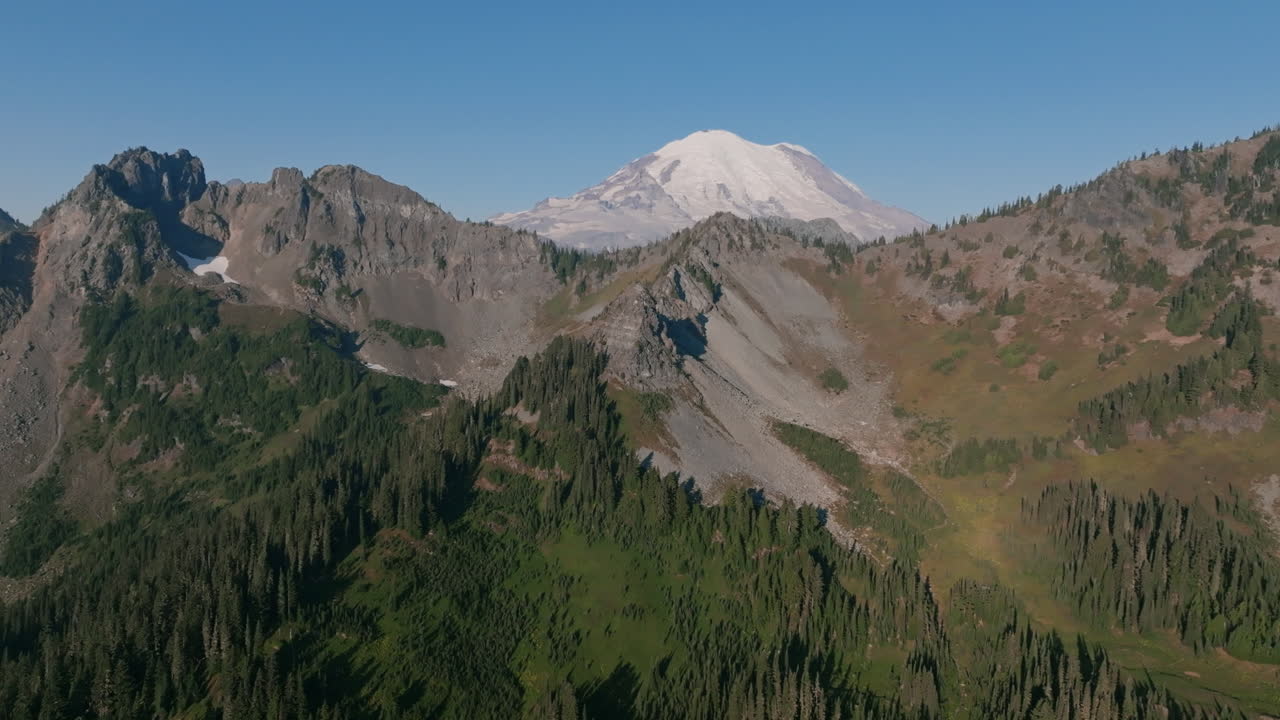 Aerial footage of a foothill in the Cascade Mountains with evergreen trees and granite rocks with Mount Rainier in the background in the morning