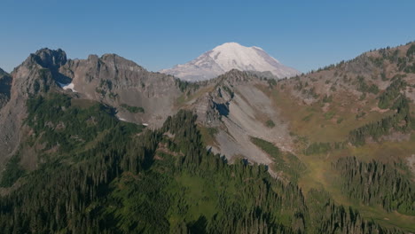 aerial footage of a foothill in the cascade mountains with evergreen trees and granite rocks with mount rainier in the background in the morning