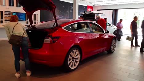 360 degree shot of red tesla model 3 being inspected by prospective buyers in tesla store at stanford shopping center in 2018, california, usa