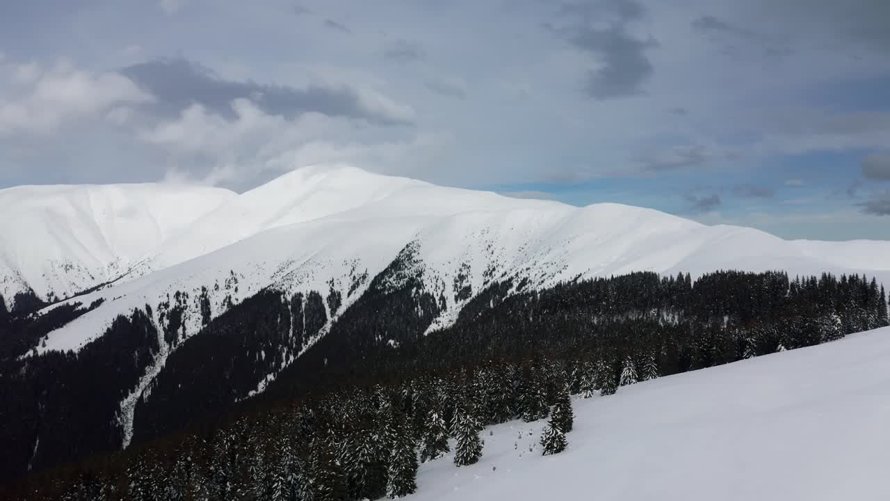 Snow-covered Papusa Peak with cloud-draped Iezer-Papusa Mountains in Romania, evergreen contrast
