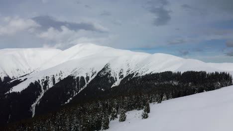 Snow-covered-Papusa-Peak-with-cloud-draped-Iezer-Papusa-Mountains-in-Romania,-evergreen-contrast